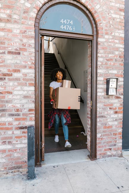 A man and a woman are engaged in a moving activity outside a building, with the man leaning forward and smiling at the woman, who is also smiling back. They are holding a cardboard box with a red and 